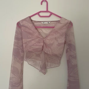 Rosa mesh blus med marmorprint - Säljer en transparent rosa meshblus från KT i storlek S. Blusen har ett unikt marmorliknande mönster, v-ringning och rynkad detalj framtill. Långa ärmar och asymmetrisk nederkant ger en cool och trendig look. Perfekt för dig som gillar statement-plagg!