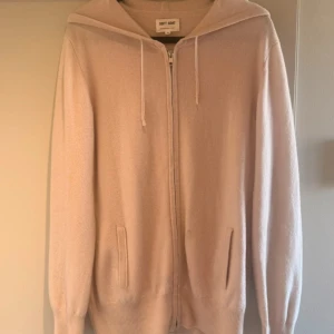 Beige hoodie i kashmir från Soft Goat - Mysig beige hoodie från Soft Goat i 100% kashmir. Tröjan har dragkedja framtill, huva med snörning och två fickor. Perfekt för dig som gillar en clean och stilren look med lyxig känsla. Passar lika bra till jeans som till mjukisbyxor.