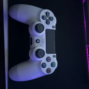 Sony DualShock 4 Wireless Controller (CUH-ZCT2E) - Vit Sony DualShock 4 trådlös handkontroll till PlayStation 4. Modellen CUH-ZCT2E. Kontrollen är i gott skick med mindre tecken på normalt bruk, inga synliga större skador. Perfekt för gaming med responsiva knappar och touchpad. Den har stick drift på en av joysticksen 