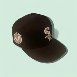 Svart White Sox keps från New Era - Snygg svart keps från New Era med broderad White Sox-logga i silver framtill och baseballspelare på sidan. Klassisk form med böjd skärm och broderade detaljer. Perfekt för dig som gillar sportig streetstyle och vill representera ditt lag.