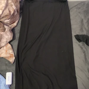 Svart långklänning från H&M Divided - En stilren svart långklänning från H&M Divided i storlek M. Klänningen har en enkel och rak passform, är ärmlös och tillverkad i mjuk, stretchig polyester. Perfekt för dig som gillar minimalistisk och clean stil.