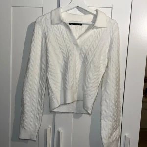 Vit kabelstickad tröja med krage - Säljer en vit kabelstickad tröja från Zara med klassisk krage och v-ringning. Tröjan har lång ärm och ribbade muddar, perfekt för lager på lager. Snygg och enkel att matcha till jeans eller kjol. Storlek L men passar ungefär storlek XS-M