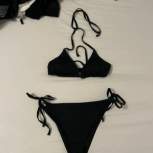 Svart bikini från Lager 157, storlek S - Snygg svart bikini från Lager 157 i storlek S. Klassisk trekantsmodell med knyt både i nacken och ryggen samt på sidorna av bikinitrosan. Stilren och enkel design som är perfekt för stranden. Materialet är mjukt och följsamt syntet.