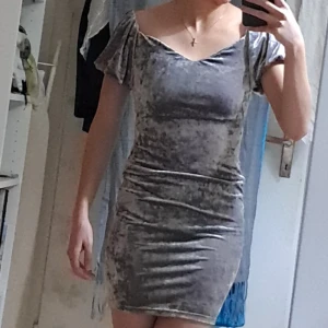 Grå sammetsoffshoulder kortklänning - Supersnygg kort klänning i grå sammet med offshoulder och lätt puffiga korta ärmar. Tight passform som framhäver figuren och v-ringad halsringning. Perfekt för dig som vill sticka ut med en cool och trendig look.