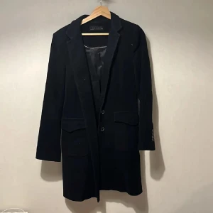 Kappa - Stilren svart lång kappa från Zara Woman med klassisk krage och två framfickor med lock. Kavajen har knäppning framtill med två knappar och dekorativa knappar vid ärmslut. Perfekt för en dressad look.