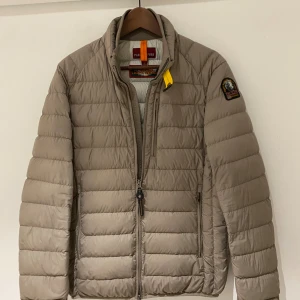 Beige pufferjacka Parajumpers S - Snygg beige pufferjacka från Parajumpers i storlek S. Jackan har quiltad design, dragkedja framtill och cool gul detalj vid kragen. Märkespatch på ärmen och flera praktiska fickor. Perfekt för dig som vill ha en lätt och stilren jacka. Ny pris 4999kr. 100% authentic.