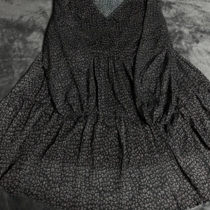 Svart leopardmönstrad klänning X&Z - Svart kortklänning från X&Z med grått leopardmönster. Klänningen har v-ringad hals, lätt rynkade detaljer i midjan och är tillverkad i en luftig mix av bomull och polyester. Perfekt för dig som gillar djurmönster och vill sticka ut.