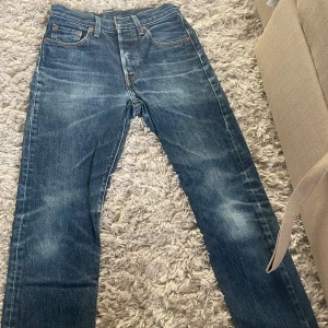 Levi's 501 blå jeans straight fit - Klassiska Levi's 501 jeans i blå denim med raka ben och femficksmodell. Snyggt slitna detaljer och ikonisk läderpatch bak. Perfekta för dig som gillar tidlös stil och vill ha ett par jeans som funkar till allt. Dom är ganska rätt jätte små för en person som är 172cm elller högre men skulle passa en person som är 160-165cm. Pris kan diskuteras(längden på byxorna är 94cm