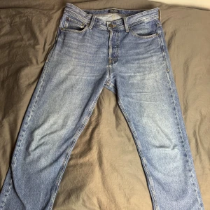 Blå jeans från Jack & Jones, 32/32 - Klassiska blå jeans från Jack & Jones i modellen Jeans Intelligence. Jeansen har fem fickor, raka ben och snygga kontrastsömmar. Tillverkade i slitstarkt bomullsjeans med en ljus tvätt som ger en avslappnad vibe. Perfekta för dig som gillar en tidlös look.