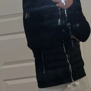 Svart cardigan från alexandro zanvetti - Svart pufferjacka från Axel Arigato med quiltad front, huva och silverfärgade dragkedjor. Jackan har långärmade släta ärmar, två sidofickor med dragkedja och en snygg logotyp på vänster ärm. Perfekt för dig som gillar stilren och modern look. Passar dig som är från 173-180