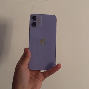 iPhone 12 mini - Snygg lila iPhone 12 med dubbla kameror och LED-blixt. Mobilen ser ut att vara i mycket gott skick utan synliga repor eller skador. Perfekt för dig som vill ha en kraftfull och stilren smartphone med modern design och hög prestanda.