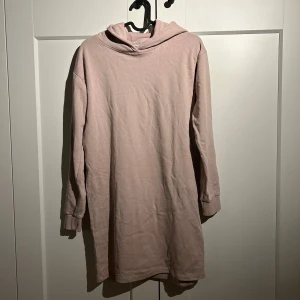 Ljusrosa hoodieklänning från Name It - Mysig ljusrosa hoodieklänning från Name It med lång ärm och huva. Klänningen är i mjuk bomull och har en avslappnad passform. Den är väldigt skön att ha på sig samtidigt som den värmer. Perfekt för mysiga dagar. 