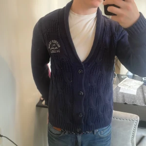 Vintage stickad Hilfiger cardigan - Väldigt fin vintage stickad Tommy Hilfiger cardigan. Passar bra nu till kallare väder. Modellen är 180cm, 73kg. Priset går att diskutera så tveka inte på att skicka iväg ett prisförslag!