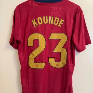 FC Barcelona Koundé 23 matchtröja Nike - Säljer en unik FC Barcelona fotbollströja från Nike med Koundé och nummer 23 på ryggen. Tröjan är röd med gula detaljer, klubbmärke och sponsortryck på bröstet. Tillverkad i lätt och ventilerande material, perfekt för match eller träning.