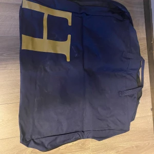 Stor marinblå förvaring väska från hööks - Säljer en stor marinblå resväska i tyg med praktiska handtag och karbinhakar. Väskan har en stor gul bokstav på framsidan och är perfekt för att packa mycket. Enkel design och rymlig insida gör den smidig att använda att ha på boxdörren eller vid tävling.