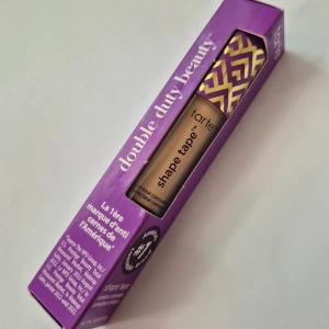 Tarte Shape Tape Concealer 29N, Travel size - Shape Tape Concealer från Tarte i nyansen 29N light-medium. Kommer i en snygg lila förpackning med guldmönstrad kork. Perfekt för att täcka mörka ringar och ge ett jämnt resultat. Travel size: Innehåller 1ml och är lätt att applicera med den mjuka applikatorn.