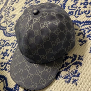 Blå keps från Gucci med GG-mönster - Snygg blå keps från Gucci med det klassiska GG-monogrammet över hela kepsen. Tillverkad i Italien och har en böjd skärm. Materialet är robust och känns lyxigt, perfekt för dig som vill sticka ut med designerstil.