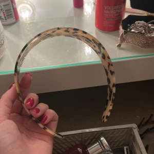 Bred diadem med leopardmönster - Snyggt och trendigt diadem i plast med bred form och leopardmönster i beige och svart. Perfekt accessoar för att lyfta din look och hålla håret på plats. Diademet har små taggar på insidan för extra grepp.
