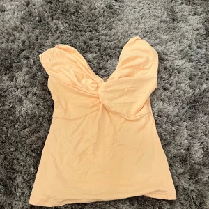 Beige offshoulder topp med twist - Säljer en snygg beige offshoulder topp med twistad detalj framtill. Toppen är figurnära och har en mjuk, stretchig känsla som sitter skönt mot kroppen. Perfekt för dig som gillar en feminin och trendig look med axlarna bara.