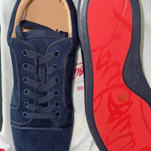 Mörkblå sneakers från Louboutin - Snygga mörkblå sneakers från Louboutin med lyxig mocka och klassisk röd sula. Skorna har rund tå, platt sula och snörning framtill. Perfekt för dig som vill sticka ut med exklusiv design och grym komfort.