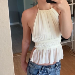 Vit omlott halterneck blus - Säljer en vit blus med halterneck och omlottkänsla. Toppen har plisserad, luftig design och markerad midja med volang nertill. Perfekt för dig som gillar en feminin och trendig look. Använt 2 ggr köpte för 70 kr
