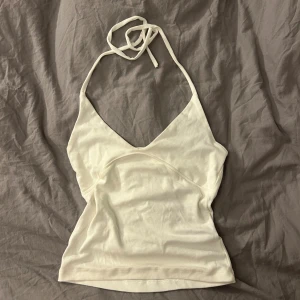 Vit omlott halterneck topp Lager 157 - Säljer en vit omlott halterneck topp från Lager 157, modell IRMA. Toppen har knyt i nacken och en snygg v-ringad front. Mjuk och stretchig bomull som sitter skönt mot kroppen. Perfekt för varma dagar och chill outfits.