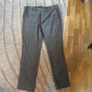 Rutmönstrade kostymbyxor från Morris - Snygga grå och svarta kostymbyxor från Morris med diskret rutmönster. Klassisk rak passform, bälteshällor och bakficka med knapp. Fodret har paisleymönster och byxorna är tillverkade i ullblandning för en dressad look.