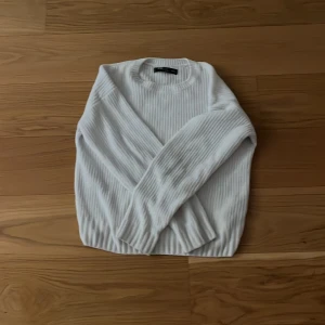 Vit ribbad stickad tröja från New Yorker  - Säljer en vit stickad tröja från New Yorker i storlek XXS. Tröjan har ett ribbat mönster, rund halsringning och långa ärmar. Perfekt för dig som gillar enkel och clean stil. Materialet är mjukt och skönt, passar till många olika outfits.