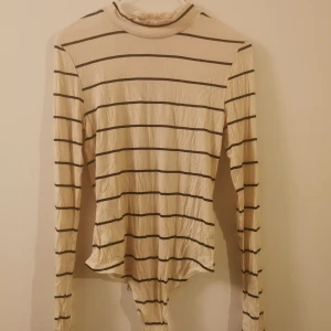 Randig body med polo från H&M - Säljer en randig body med polo från H&M. Toppen är långärmad och har en ribbad struktur samt hög hals. Materialet är 95% LivaEco viskos, vilket gör den mjuk och skön mot huden. Oanvänd. 