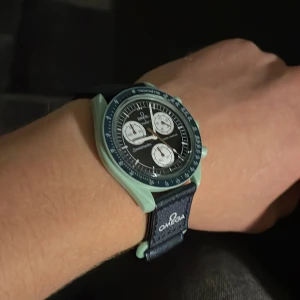 Omega x Swatch Speedmaster MoonSwatch - Säljer en Omega x Swatch Speedmaster MoonSwatch Mission on Earth med mintgrönt boett, svart urtavla och vita subdials. Klockan har en mörkblå textilrem med Speedmaster-tryck och detaljerad baksida med jordmotiv. Perfekt för dig som gillar cool design och ikoniska samarbeten. Har kronograf funktionen! Pris satt då jag inte har orginal lådan till klockan!