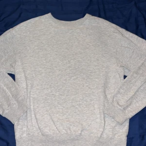 Ljusgrå sweatshirt i bomull - En basic ljusgrå sweatshirt med rund hals och långa ärmar. Tröjan har ribbade muddar vid ärmslut och nederkant, vilket ger en klassisk och avslappnad look. Perfekt att slänga på sig när det är lite kyligare ute.