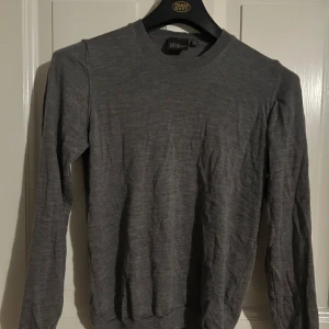 Grå merinoulltröja från Oscar jackobsson - Snygg grå långärmad tröja från Oscar jackobsson i mjuk merinoull. Rund halsringning och ribbade muddar vid ärmslut och nederkant. Perfekt för dig som gillar stilrena och enkla plagg med skön passform.