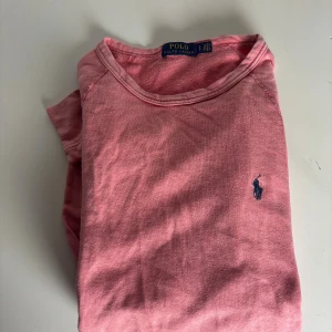 Rosa långärmad tröja från Polo Ralph Lauren - Snygg rosa långärmad tröja från Polo Ralph Lauren med klassisk rund hals och mörkblå broderad logga på bröstet. Tillverkad i mjuk bomull som är skön mot huden. Perfekt för dig som gillar stilrena och bekväma plagg med en sportig touch.