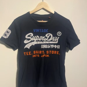 Superdry mörkblå t-shirt - Mörkblå Superdry t-shirt med tryck framtill och en stor vit siffra 23 på ena ärmen.  Skick: Gott skick, sparsamt använd.  Storlek: M men passar S bättre  Kolla gärna in mina andra annonser.   Skriv vid frågor eller ifall du vill ha fler bilder. 