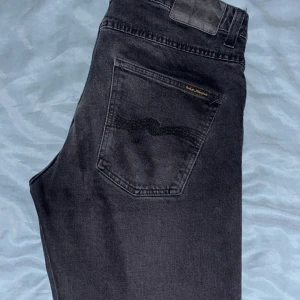 Nudie jeans-grim Tim  - Snygga svarta jeans från Nudie Jeans, storlek 31/32 i modellen grim Tim, byxorna har en klassisk femficksdesign och diskret logga på bakfickan. Jeansen har en rak passform och är tillverkade i mjukt denimtyg med lätt tvättad look. Perfekt för dig som gillar stilrena och tidlösa jeans. Modellen på bilderna är 187 och väger 69kg, 