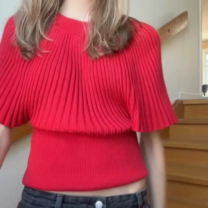 Röd ribbad topp med vida ärmar - Säljer en röd ribbad topp med korta, vida ärmar och rund halsringning. Toppen har en croppad passform och är tillverkad i ett stretchigt stickat material som sitter snyggt på kroppen. Perfekt för dig som vill ha en färgstark och trendig look.