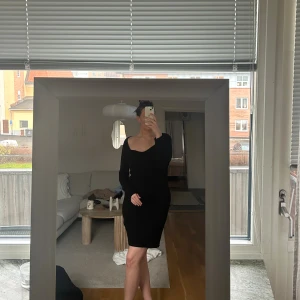 Svart ribbad klänning från Vero moda - Säljer en svart, ribbad klänning från Vero moda med lång ärm och v-ringad hals. Klänningen är figurnära och har en kort längd som ger en clean och modern vibe. Passar för dig som gillar minimalistisk stil och vill ha något som är både bekvämt och stilrent.