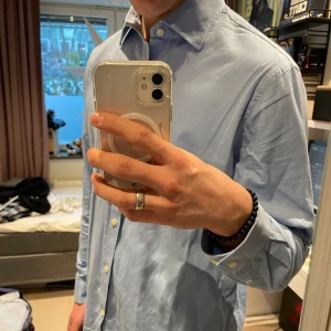 Blå skjorta Michael Kors - Snygg ljusblå skjorta från Michael Kors. Skjortan har klassisk krage, långa ärmar med manschett och vita knappar framtill. Tillverkad i mjuk bomull som känns skön mot huden. Storlek XL ger skön loose passform på mig som bär M. Perfekt för dig som gillar stilrena och fräscha plagg.