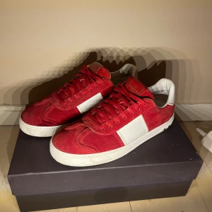 Valentino flycrew röda  - Snygga Valentino Rockrunner sneakers i rött mocka med vita skinnpaneler och vita detaljer. Skorna har snörning, rund tå och platt sula med camouflage-mönster undertill. Bak på hälen finns små nitar för extra edge. Perfekt för dig som gillar exklusiva streetwear-vibbar.