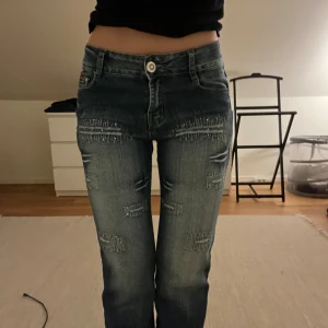 Jeans med detaljer  - Säljer ett par mörkblå H&L jeans med bootcut passform och mid midja. Jeansen har snygga slitningar och dekorativa detaljer med nitar på framsidan. Size 28                                                                        Midja: 70 cm  Innebenslängd: 78 cm  Ytterbenlängd: 103 cm  Höftvidd: 50 cm  Benslut: 22 cm