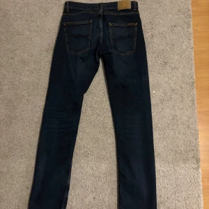 Mörkblå jeans från Nudie Jeans - Snygga mörkblå jeans från Nudie Jeans med klassisk femficksdesign och kontrastsömmar. Jeansen har modellen grim tim och strl w31 L32