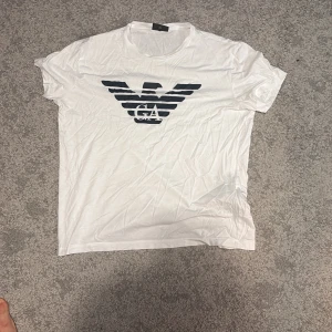 Vit Emporio Armani t-shirt XXL/ vuxen S - Passar som vuxen S. Snygg vit t-shirt från Emporio Armani i storlek XXL. Framsidan har det klassiska svarta EA-logotrycket med örn, rund hals och korta ärmar. Materialet är mjukt och skönt bomull, perfekt för en clean och stilren look.