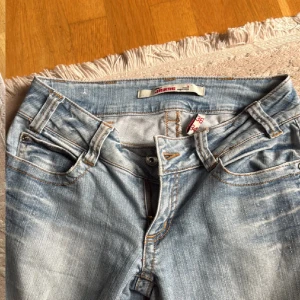 Ljusblå bootcut jeans från Jeans - Säljer ett par ljusblå bootcut jeans från Jeans i klassisk femficksmodell. Jeansen har låg midja, snygga slitningar och kontrastsömmar. Perfekta för dig som gillar en avslappnad och trendig look.