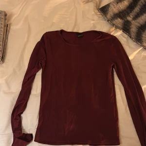 Vinröd långärmad tröja Gina Tricot - En enkel och stilren vinröd långärmad tröja från Gina Tricot. Tröjan har rund halsringning och är gjord i ett mjukt, tunt material som känns skönt mot huden. Perfekt att matcha med jeans eller kjol för en clean look.