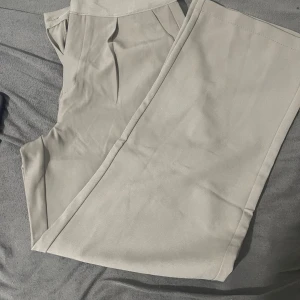 Beige kostymbyxor, storlek M -  Beige kostymbyxor från 157 i storlek M. Byxorna har raka ben och klassisk passform med pressveck framtill. Perfekt för dig som gillar stilrena och enkla plagg. Materialet känns mjukt och har en lätt stretch för extra komfort.