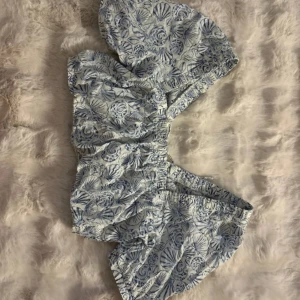 Blåvit topp med snäckmönster - Säljer en blåvit topp med elastisk midja och snyggt snäckmönster. Perfekta för varma dagar och strandhäng. De har en lös passform och är tillverkade i ett lätt bomullstyg som känns skönt mot huden.