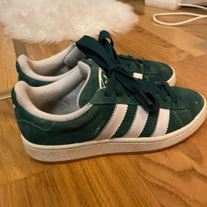 Gröna Adidas campus - Säljer mina fina Adidas campus då de är för stora för mig och därmed också inte kommer till användning! Dem är i väldigt bra skick med nästan inga tecken på användning. Den vita pricken på högra skons främre del är endast en liten lövbiff som jag nu tagit bort! 😅. Skorna har används varsamt och försiktigt. Vid seriös köpare kan jag skicka flera bilder 🫶pris går också att diskutera!