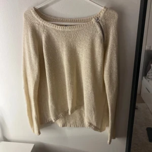 Beige stickad tröja med dragkedja - Snygg beige stickad tröja med rund hals och cool detalj i form av en dragkedja vid axeln. Tröjan har långärmade och en avslappnad passform som gör den perfekt för lager-på-lager. Enkel att matcha med jeans eller kjol för en chill look.