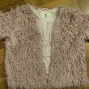 Ljusrosa pälsjacka från H&M - Säljer en fluffig ljusrosa pälsjacka från H&M i storlek 146/152. Jackan har en öppen front utan knappar eller dragkedja och är tillverkad i syntetmaterial med ett mjukt, lockigt yttre. Perfekt för dig som vill sticka ut med en cozy vibe.