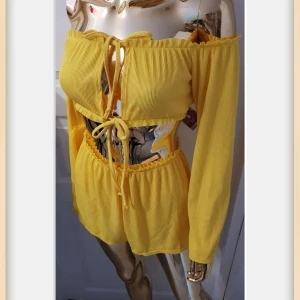 Oanvänt Gult set från Boohoo - Snygga set med Top och shorts från Boohoo i ribbat material med elastisk midja och snörning framtill shortsen. De är höga i midjan och har en luftig, loose passform som passar perfekt till tex varma dagar. Materialet är mjukt och lätt, vilket gör dem superbekväma.